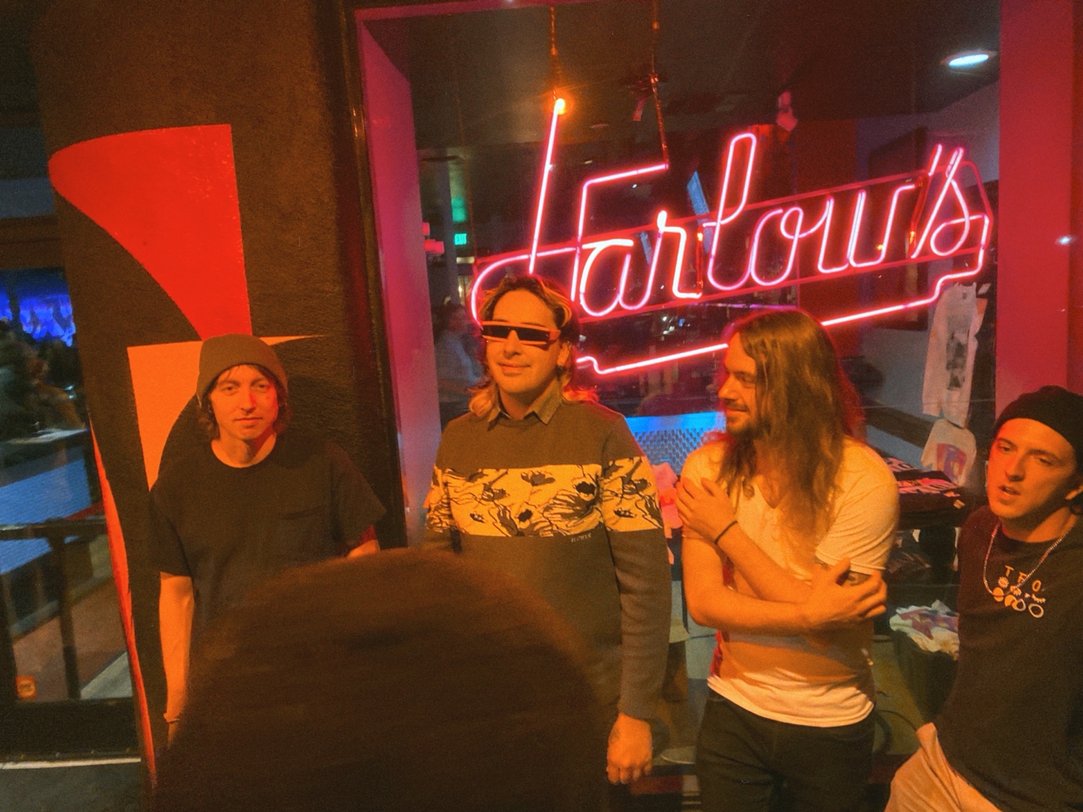 Band members standing beneath a neon sign